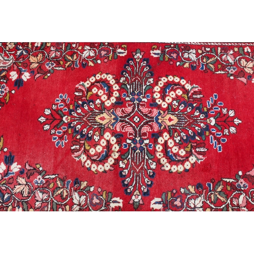 566 - A Persian rug - with a large floral medallion and spandrels on a madder ground, within a blue floral... 