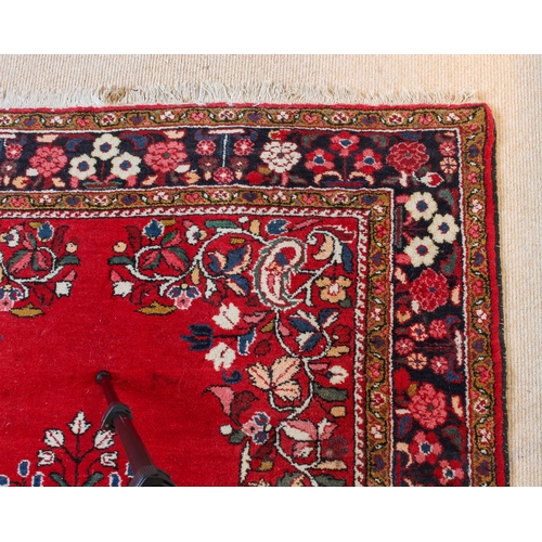 566 - A Persian rug - with a large floral medallion and spandrels on a madder ground, within a blue floral... 