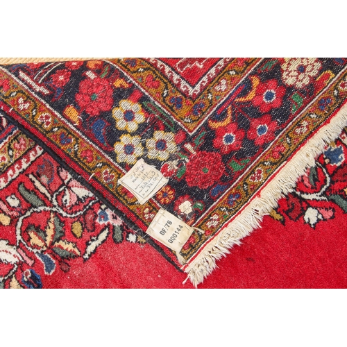 566 - A Persian rug - with a large floral medallion and spandrels on a madder ground, within a blue floral... 