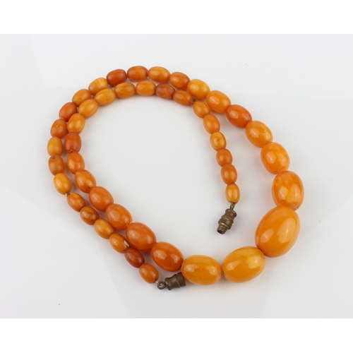 201 - An antique egg yolk amber bead necklace - the oval beads graduating from 6.5mm to 17mm long, with br... 