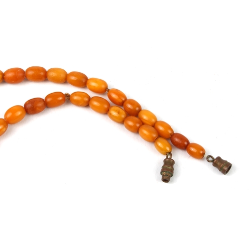 201 - An antique egg yolk amber bead necklace - the oval beads graduating from 6.5mm to 17mm long, with br... 