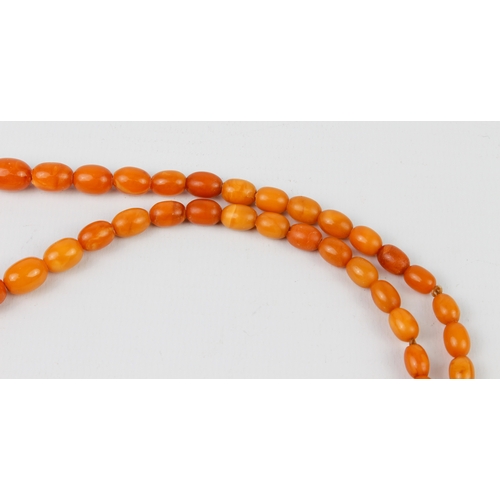 201 - An antique egg yolk amber bead necklace - the oval beads graduating from 6.5mm to 17mm long, with br... 