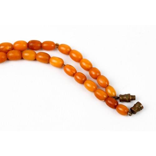 201 - An antique egg yolk amber bead necklace - the oval beads graduating from 6.5mm to 17mm long, with br... 