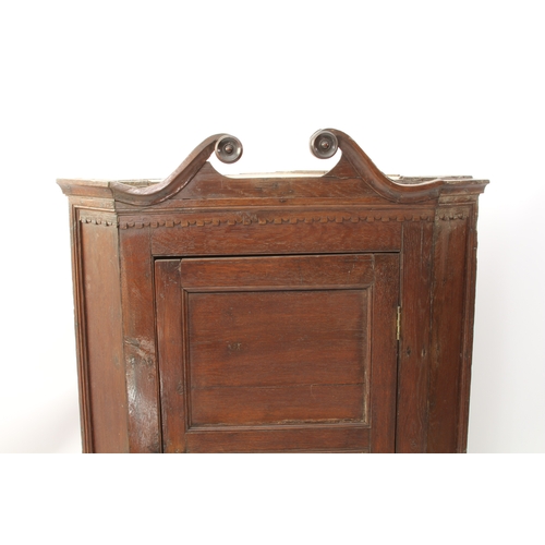 471 - A George III oak hanging corner cupboard - the swan-neck cornice over a dentil frieze and two-panel ... 