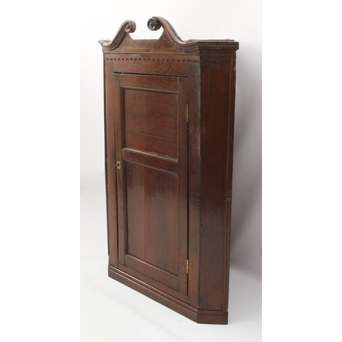 471 - A George III oak hanging corner cupboard - the swan-neck cornice over a dentil frieze and two-panel ... 