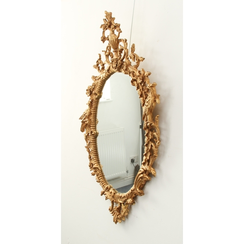 573 - A George II style carved gilt wood mirror - late 20th century, the oval plate within a floral and fo... 