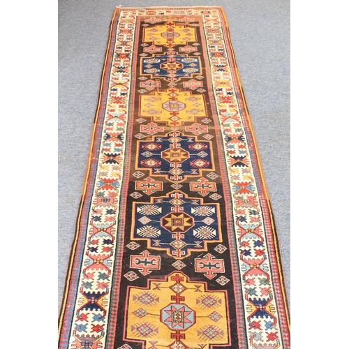 622 - A good Kazak runner - c.1900, with nine central lozenge medallions in blue and deep yellow on a dark... 