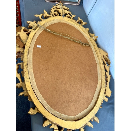 573 - A George II style carved gilt wood mirror - late 20th century, the oval plate within a floral and fo... 