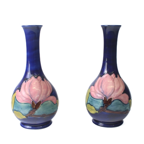 9 - A pair of Moorcroft 'Magnolia' pattern bottle vases - the pink flowers on a dark blue ground, one wi... 