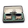A cased pair of silver Mustard Pots, and spoons, with pierced decorated bodies and blue glass liners... 