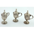 A set of three Georgian period urn shaped Mustard or Condiment Pots, the hinged lids with reeded des... 