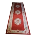 A set of three red/pink ground woollen Runners, each with a cream ground floral border and three cen... 