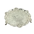 A silver Salver, London, with scrolling rim interspersed by shells, embossed centre on three hoof fe... 