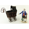 A miniature cane-work Dolls Pram, with canvas top and metal undercarriage; and a Continental porcela... 