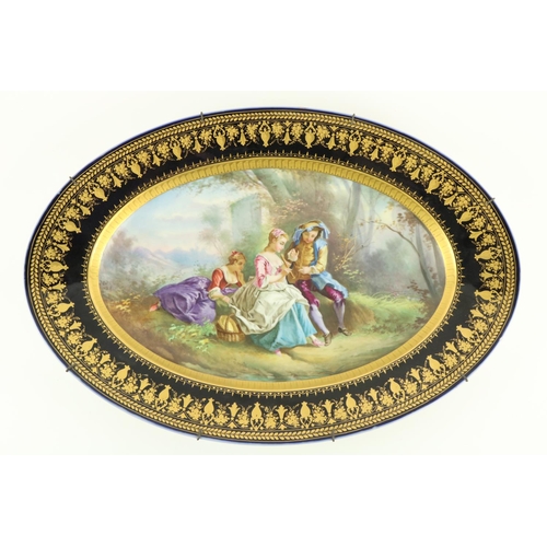 259 - A large oval Serves style porcelain Platter, depicting three figures in a garden landscape, inside a... 