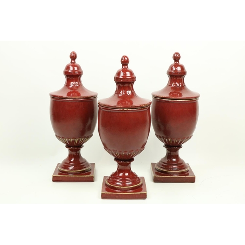 351 - A set of 3 large burgundy ground ceramic Urns and Covers, each on square stem base. (3)... 