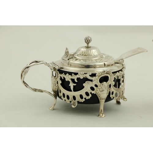 64 - An ornate Victorian silver Mustard, in the rococo style, with leaf cast handle and hinged cover, enc... 