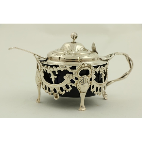 64 - An ornate Victorian silver Mustard, in the rococo style, with leaf cast handle and hinged cover, enc... 