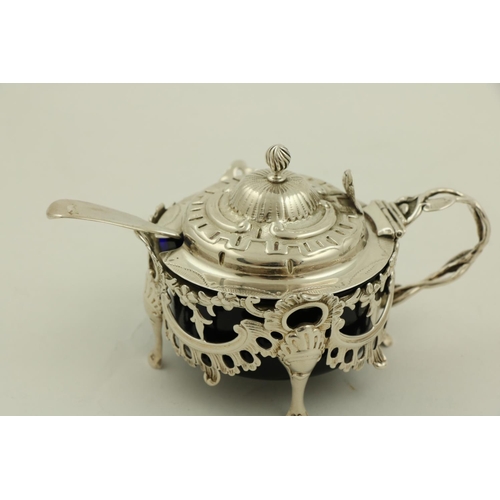 64 - An ornate Victorian silver Mustard, in the rococo style, with leaf cast handle and hinged cover, enc... 