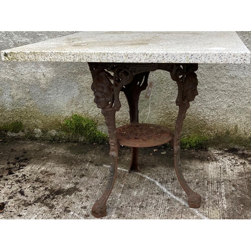 1352 - A cast iron tripod Cricket Table, the legs headed with classical mask and a square faux granite top,... 