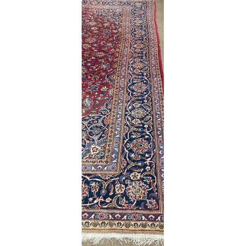 656 - A large Middle Eastern burgundy ground woollen Carpet, the central panel with floral medal... 