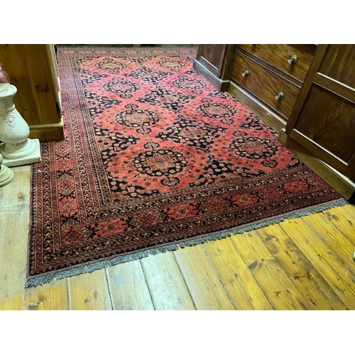 425 - An attractive Middle Eastern woollen Carpet, the centre with eleven medallions on burgundy ground in... 