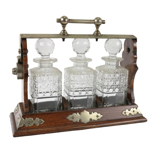 292 - An nearly Edwardian brass mounted oak Tantalus, with three original cutglass decanters and stoppers.... 