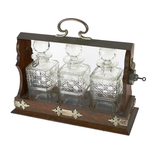 295 - An Edwardian oak cased metal mounted Tantalus, housing three cutglass bottles and stoppers. (1)... 