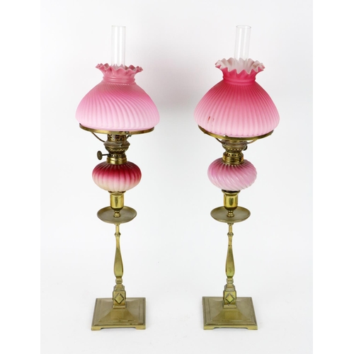 485 - A pair of brass Candlesticks, each fitted with a pink reeded glass Oil Lamp, with matching pink glas... 