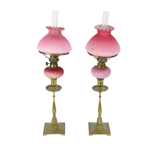 485 - A pair of brass Candlesticks, each fitted with a pink reeded glass Oil Lamp, with matching pink glas... 