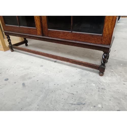 614 - A large antique oak glazed 2 door bookcase with carved decoration and Barley Twist legs