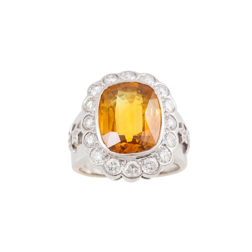 303 - AN ORANGE SAPPHIRE AND DIAMOND CLUSTER RING, the cushion cut sapphire to a brilliant cut diamond sur... 