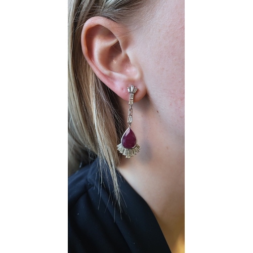 126 - A PAIR OF RUBY AND DIAMOND DROP EARRINGS, the baguette cut diamond lines suspending pear shaped rubi... 