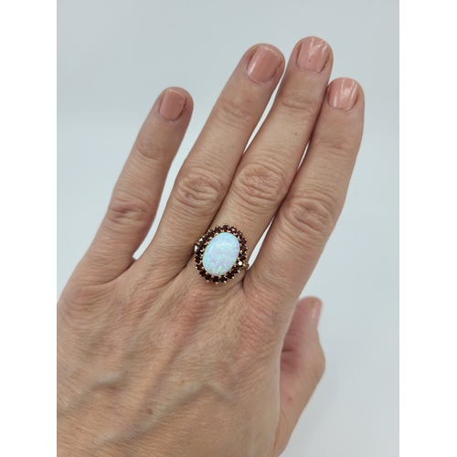 28 - A SYNTHETIC OPAL AND GARNET SET CLUSTER RING, the central synthetic opal to garnet set surround, mou... 