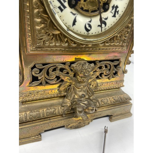 599 - A PIERCED BRASS MANTLE CLOCK WITH A CHERUB FIGURE TO BASE AND WHITE PORCELAIN DIAL