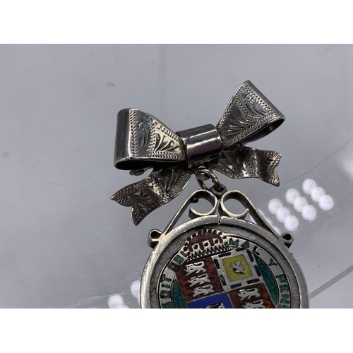 214 - AN 1887 SILVER AND ENAMEL COIN SUSPENDED FROM A SILVER BOW BROOCH