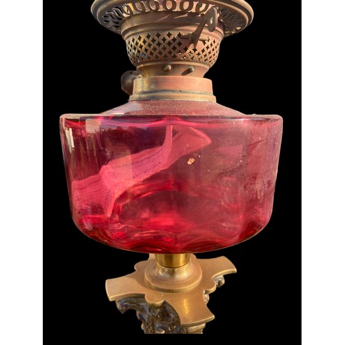 682 - A VICTORIAN ORNATE BRASS CORINTHIAN PILLARED OIL LAMP WITH A SHAPED RUBY BOWL COMPLETE WITH FUNNEL (... 