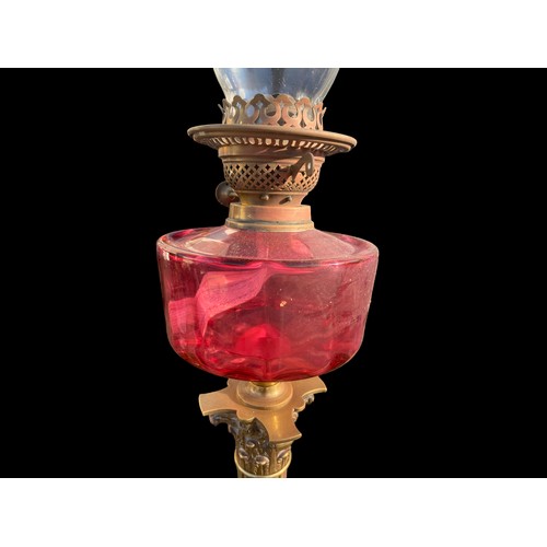 790 - A VICTORIAN ORNATE BRASS CORINTHIAN PILLARED OIL LAMP WITH A RUBY BOWL COMPLETE WITH FUNNEL