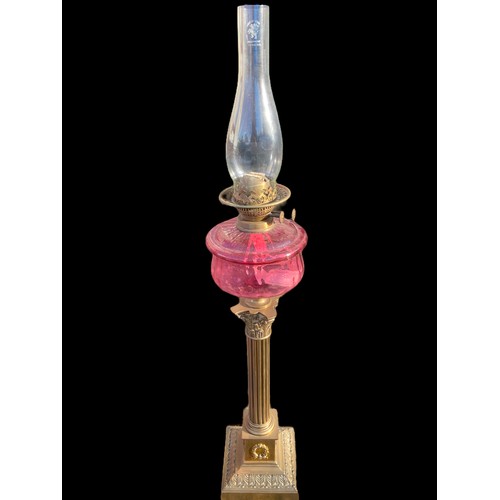 790 - A VICTORIAN ORNATE BRASS CORINTHIAN PILLARED OIL LAMP WITH A RUBY BOWL COMPLETE WITH FUNNEL