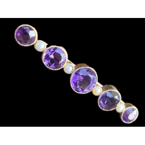 517 - A BROOCH SET WITH 5 GRADUATED ROUND AMETHYST 4.5cm IN LENGTH AND 5 SEED PEARLS IN YELLOW RUBOVER SET... 