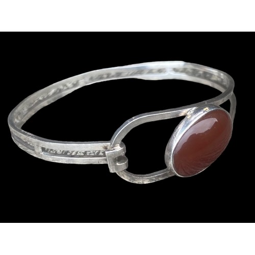 494 - AN ORNATE SILVER BANGLE SET WITH A CORNELIAN STYLE STONE