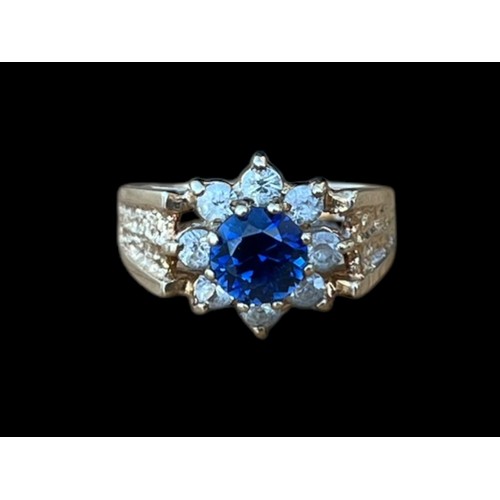 642 - A 9CT GOLD CLUSTER RING WITH A BLUE CENTRE STONE SURROUNDED BY 8 CLEAR STONES WEIGH 3.7G