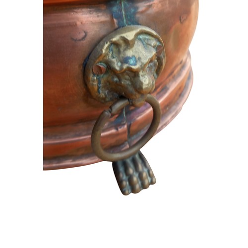 151 - A COPPER POT WITH BRASS LION HEAD HANDLES ON A TRIPOD FOOT