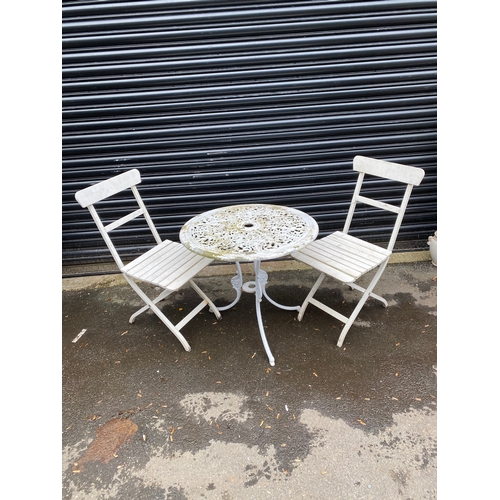 359 - White metal garden table with two white foldable chairs.