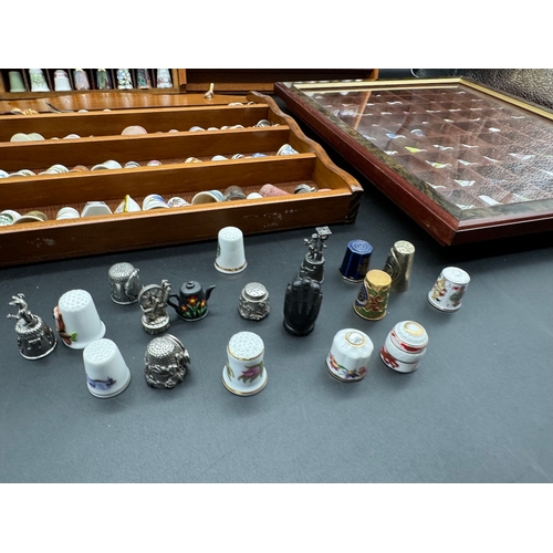 88 - Large quantity of decorative display thimbles including sterling silver thimbles on display cabinets