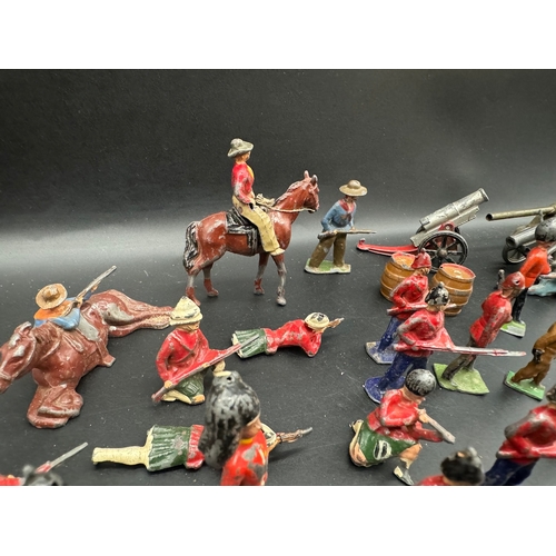 253 - A collection of early 20th century lead toy soldiers, cowboys + military badges