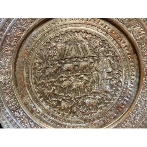 65 - A PERSIAN QAJAR SILVER TONE WALL TRAY. EMBOSSED WITH DESERT SCENE DEPICTING MUSICIAN PLAYING TO HERD... 