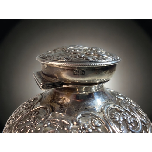 25 - AN EDWARDIAN WILLIAM COMYNS  & SONS REPOUSSÉ SILVER & CRYSTAL INKWELL, WITH WATCH HOLDER TO LID. 
LO... 