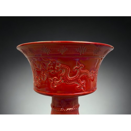 131 - A CHINESE RED GLAZE STEM VASE. RELIEF DECORATED WITH TWIN DRAGONS. GREEK KEY TO THE RIM AND TOBACCO ... 