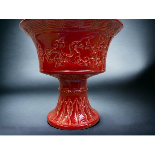 131 - A CHINESE RED GLAZE STEM VASE. RELIEF DECORATED WITH TWIN DRAGONS. GREEK KEY TO THE RIM AND TOBACCO ... 